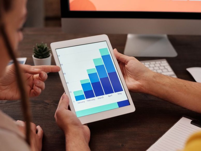 Two adults working in an office, examining graphs on a tablet screen for data analysis.