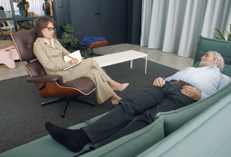 A therapist taking notes while a patient lies on a sofa during a counseling session.